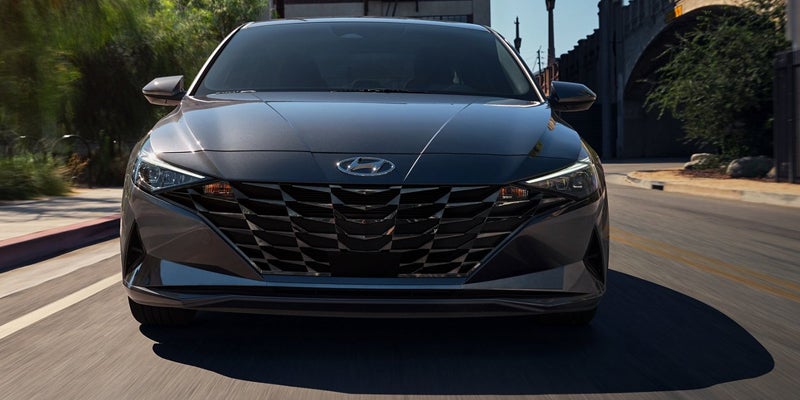 Vista frontal de un Hyundai Elantra gris oscuro circulando por una calle soleada.