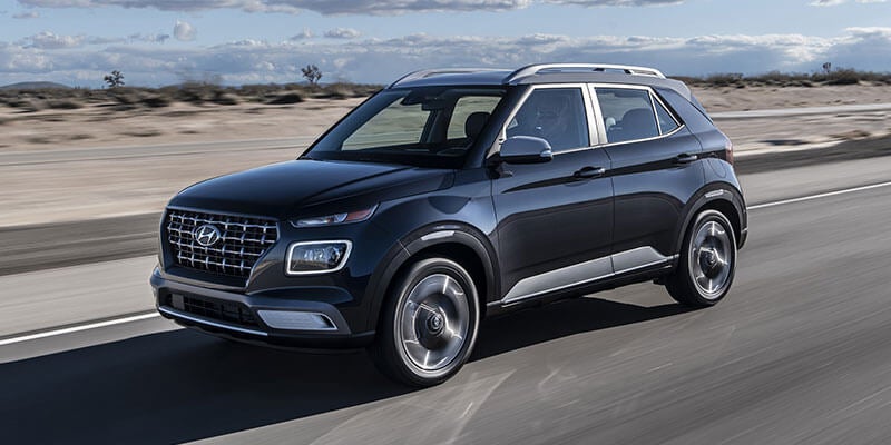 Un SUV Hyundai Venue negro circulando por una autopista a través de un paisaje desértico bajo un cielo azul con nubes dispersas.