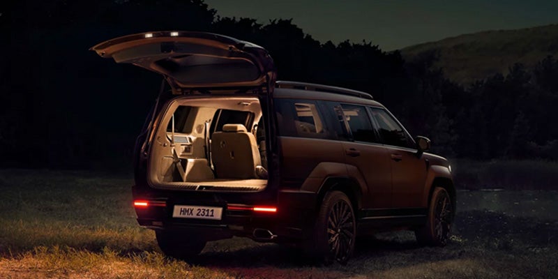 Un SUV de color marrón oscuro con el portón trasero abierto, iluminando la zona de carga por la noche en un entorno natural.