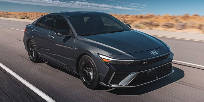 Un Hyundai Elantra N Line de color gris oscuro, visto desde arriba y ligeramente de frente, circulando por una autopista.