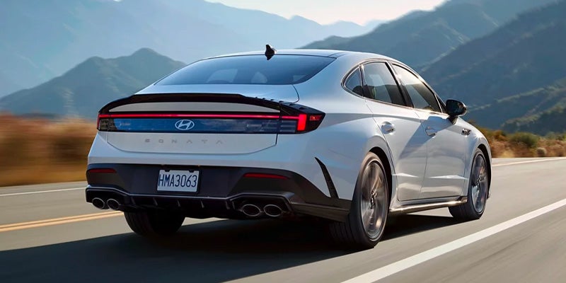 Un sedán Hyundai Sonata N Line blanco estacionado al costado de una carretera con un paisaje montañoso y vegetado de fondo.