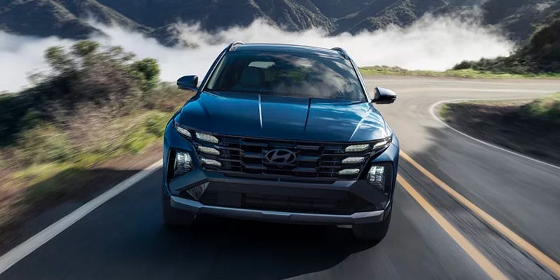 Vista frontal de un Hyundai Tucson azul oscuro circulando por una carretera de montaña con curvas y niebla al fondo.