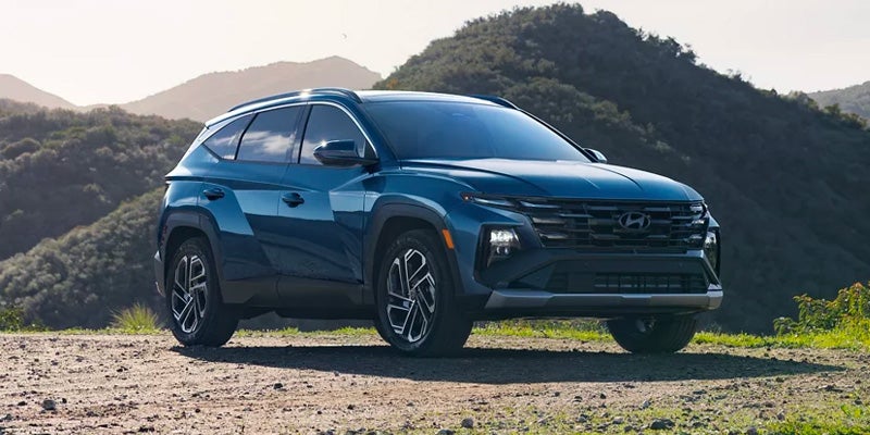 Un SUV Hyundai Tucson azul está estacionado en un camino de tierra, ligeramente inclinado hacia la derecha, con montañas detrás.