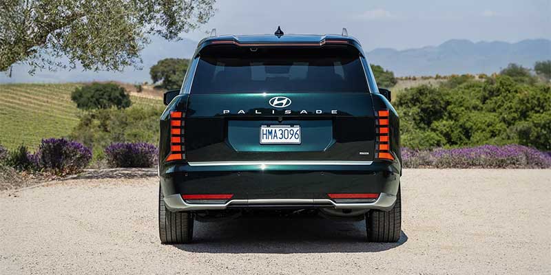 Vista trasera de un SUV Hyundai Palisade de color verde oscuro estacionado en un camino de grava con vistas a un viñedo con arbustos de lavanda.