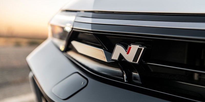 Sedán Hyundai Elantra N-Line de color gris oscuro circulando de derecha a izquierda en una autopista, mostrado desde una vista trasera de tres cuartos.