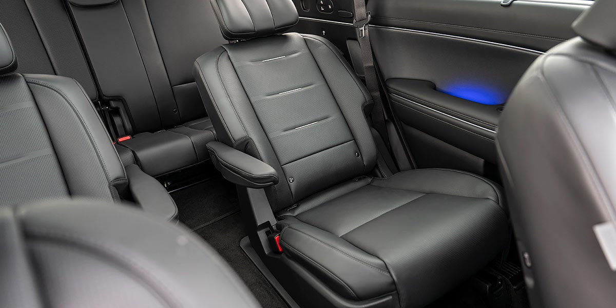 Un espacioso interior de coche con dos techos corredizos que deja ver un cielo azul despejado con algunas nubes blancas dispersas.